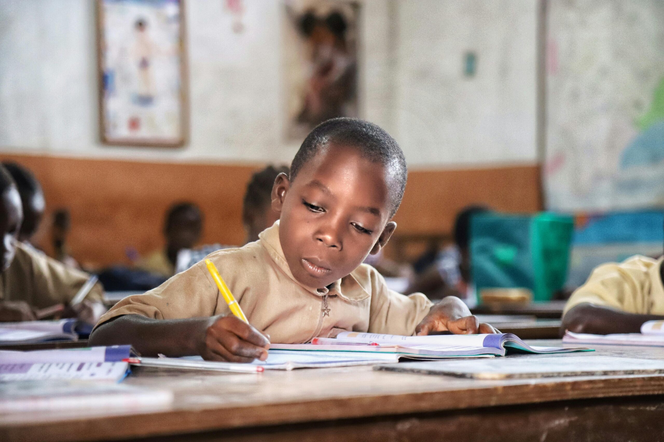 Young African boy focused on writing at his desk in a vibrant classroom setting.